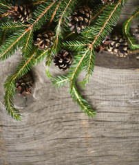 Christmas card on a wooden background with a decor of fir branches and cones.