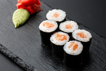 Maki Sushi Rolls with salmon on black stone on dark background. With ginger and wasabi. Sushi menu. Japanese food. Closeup of delicious japanese food with sushi roll. Horizontal photo