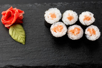 Maki Sushi Rolls with salmon on black stone on dark background. With ginger and wasabi. Sushi menu. Japanese food. Closeup of delicious japanese food with sushi roll. Horizontal photo