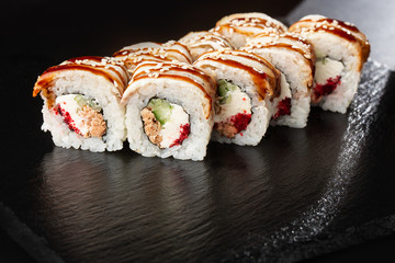 Golden dragon sushi roll. Sushi Rolls with flying fish caviar , tuna, eel, cucumber, sesame seeds and Cream Cheese inside and on black slate isolated. Horizontal
