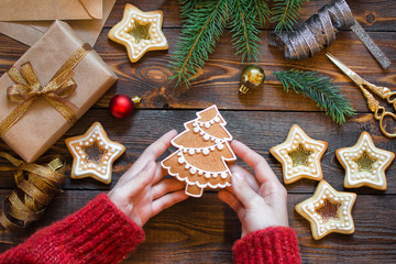 Womens hands hold a New Year's gingerbread over a wooden table with spruce branches, home-made cookies and Christmas tree toys. 