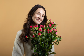 Image of a young beautiful woman posing isolated against an orange wall holding a bouquet of pink roses
