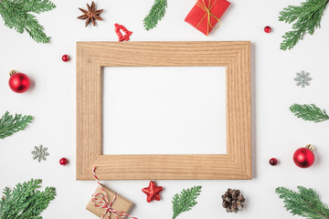 Fototapeta na wymiar Blank Christmas photo card in frame made of fir tree branches, gift boxes, red holiday decorations on white background