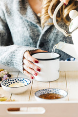 A female model is drinking herbal tea with honey for flu, she is pouring herbal tea and honey into a white enamel cup
