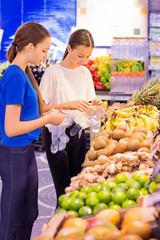 Teen girls shopping in supermarket reading product information. Choosing daily product.Concept of healthy food, bio, vegetarian, diet.