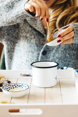 A female model is drinking herbal tea with honey for flu, she is pouring herbal tea and honey into a white enamel cup