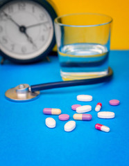 Alarm clock for the timely adoption of pills, a stethoscope, multi-colored pills, on a blue background.