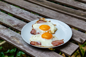 Fried eggs with bacon on the wooden table in the garden