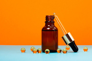Face serum and vitamin capsules on the trendy orange and blue background. Collagen, hyaluronic acid...