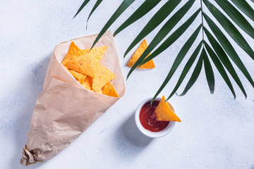 Traditional mexican snack nachos in a paper bag with sauce and a palm branch on a white background