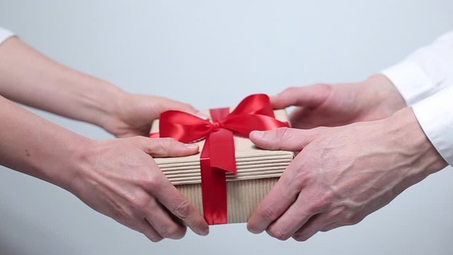 Female and male hands give a box with a gift. Holiday packaging.