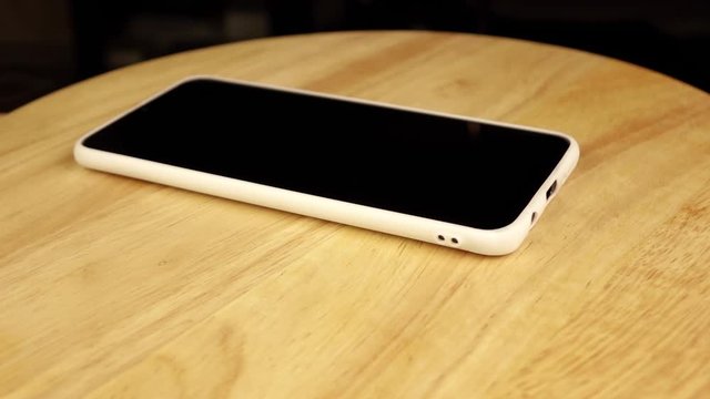 black phone in white case rotates 360 degrees on wooden stand.