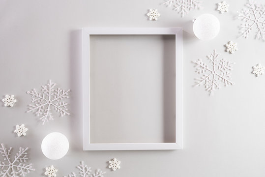 Christmas background concept. Top view of Christmas ball with picture frame and snowflakes on light gray pastel background.