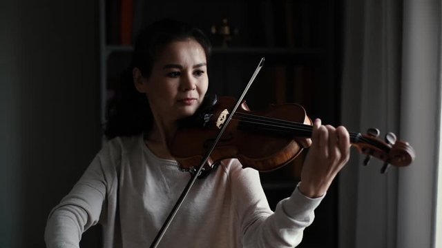 Lovely Young Woman Plays The Violin In Slow Motion In A Room With A Modern Interior. Girl Is Practicing Playing Musical Instrument At Home.