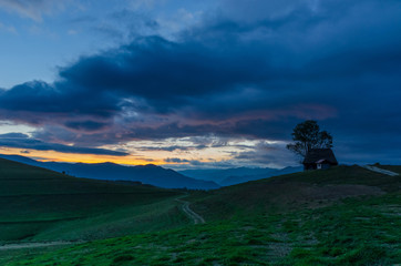 Naklejka premium Traditional houses and dramatic sky in Dumesti village, Apuseni Mountains, Romania, at sunset