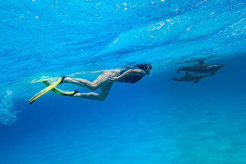 woman swimming with a pod of Spinner dolphins (Stenella longirorstris) over sand in Sataya reef,...