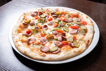 Cheap pizza with sausages, cucumbers, cherry tomatoes, and herbs.