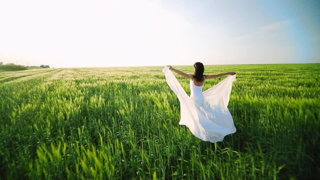 Summer or Spring concept. Freedom, wind, flight - the concept of cleanliness and change. Dancer in white fabric walk on green field.
