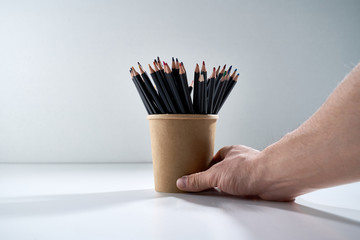 Multi-colored pencils for drawing in a brown cardboard stand on a gray background