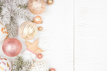 Christmas side border of snowy branches and dusty rose, gold, and white ornaments. Top view on a white wood background.