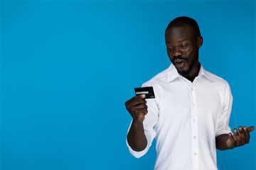Beautiful afroamerican guy looks at the credit card and shows his emotions