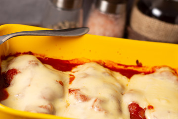 Delicious Chicken Parmigiana served in yellow baking dish with on a wooden table and stone or concrete background..