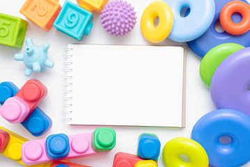 Baby toys and blank page notepad flat lay background with copy space. Toys list mockup.