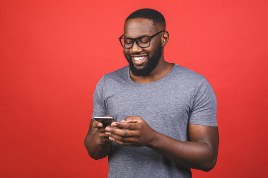 Portrait of handsome excited cheerful joyful delightful african american guy wearing casual sending and getting messages to his lover isolated against red background. Using phone.