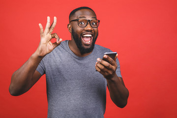 Afro american man using smartphone over isolated red background doing ok sign with fingers,...