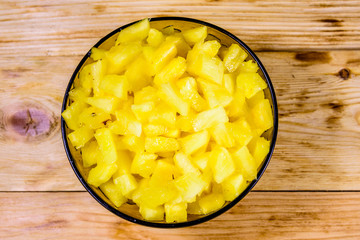 Glass bowl with chopped pineapple on wooden table. Top view