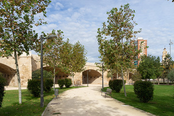 Path with bench towards ancient stone bridge across old riverbed. Puente del Real, Turia river, Valencia, Spain