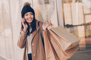 Young woman with shopping bags talking on the phone and walking near mall.