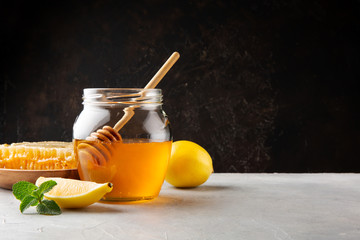 Honey in a glass jar and honeycomb, lemon and mint on a gray table and dark wall background