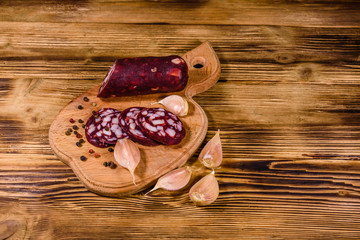 Cutting board with sliced salami sausage and garlic on a wooden table