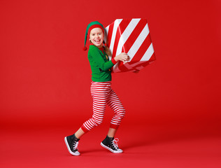 cheerful funny baby in Christmas elf costume with gifts on   red background.