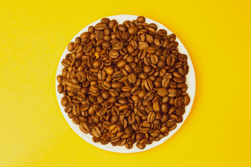 Brown coffee beans on a plate. heap of whole coffee beans on yellow background. copy space