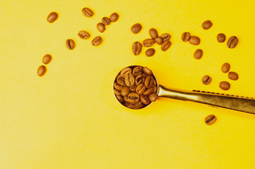Roasted coffee beans with a spoon on the yellow background