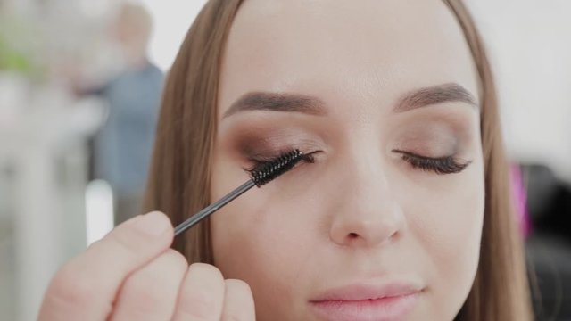Professional makeup artist woman paints eyelashes to client of beauty salon.