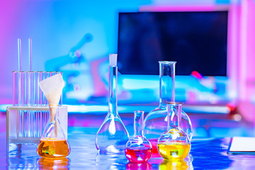 Glassware with colored chemical liquids is on the table. Flasks and test tubes on the background of a chemical laboratory. Study of the properties of herbs for the cosmetic industry.
