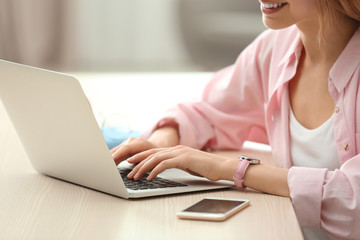 Young woman using laptop at table indoors, closeup