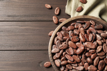 Bowl with cocoa beans on wooden table, top view. Space for text