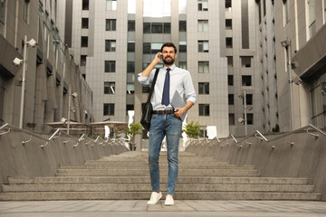 Handsome man with laptop talking on phone in city