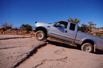 Fototapeta na wymiar A silver four wheel drive pickup truck is crawling up a rocky slope