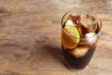 Glass of refreshing soda drink with ice cubes and lime on wooden table. Space for text
