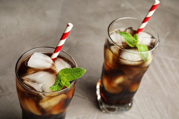 Glasses of refreshing soda drink with ice cubes and straws on grey table