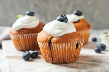 Marble board with tasty muffins, cream and blueberries on table