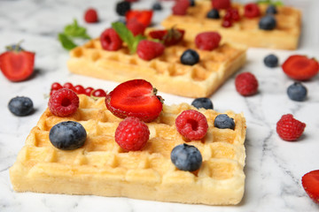 Delicious waffles with fresh berries served on white marble table, closeup