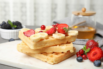Board with delicious waffles and fresh berries on kitchen table