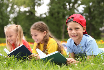 Fototapeta premium Group of little children reading books on green grass in park
