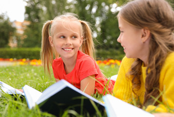Cute little girls reading books on green grass in park